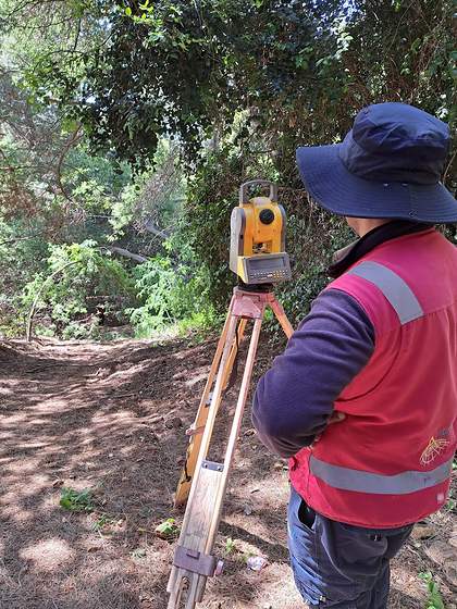 Topógrafo trasladando equipos por una huella de acceso